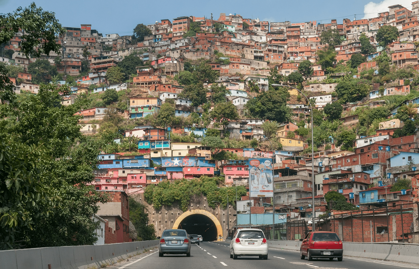 Venezuelans suffer debilitating poverty. The image here shows a Venezuelan barrio built on a hill with a freeway tunnel at the bottom.